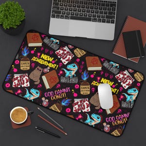 Puede incluir: Un mousepad rectangular negro con un patrón repetido de dinosaurios de dibujos animados, libros y texto. El texto incluye "NEW ACHIEVEMENT!" y "GOD DAMNIT DONUT!". El mousepad también presenta un gato con gafas de sol.