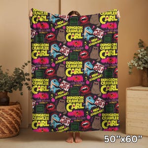 May include: A black blanket with a repeating pattern of cartoon dinosaurs, cats, and text that reads "Dungeon Crawler Carl." The blanket also features the text "New Achievement!" and "God Damnit Donut!" The blanket measures 50 inches by 60 inches.