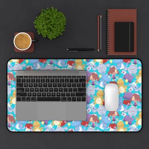 May include: A rectangular desk mat with a vibrant blue background and a repeating pattern of cartoon characters. A silver laptop, white mouse, and a keyboard are on the mat. A cup of coffee, a plant, and stationery are also on the desk.