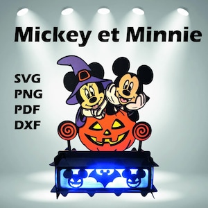 May include: A Halloween-themed light-up decoration featuring Mickey and Minnie Mouse characters. The design includes a carved orange pumpkin, a black base with blue lights, and the text "Mickey et Minnie".