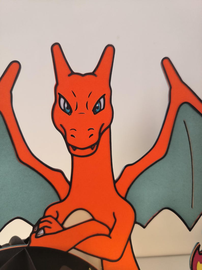 May include: A red and orange cartoon dragon with teal wings. The dragon has a fierce expression with blue eyes and a wide open mouth.