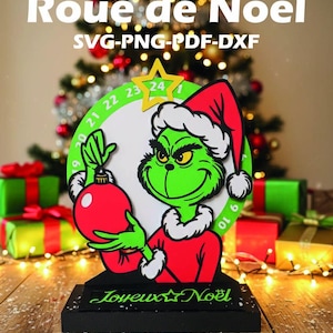 Peut inclure: Décoration de Noël avec un personnage vert tenant une boule rouge. Le personnage porte un bonnet de Père Noël et un costume rouge. Le design comprend une roue de compte à rebours avec des chiffres et le texte "Roue de Noël" et "Joyeux Noël".