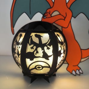 May include: A black light-up lamp shaped like a sphere with a silhouette of a dragon on the front. The lamp is lit and glowing. The lamp is next to a cartoon image of a red dragon.