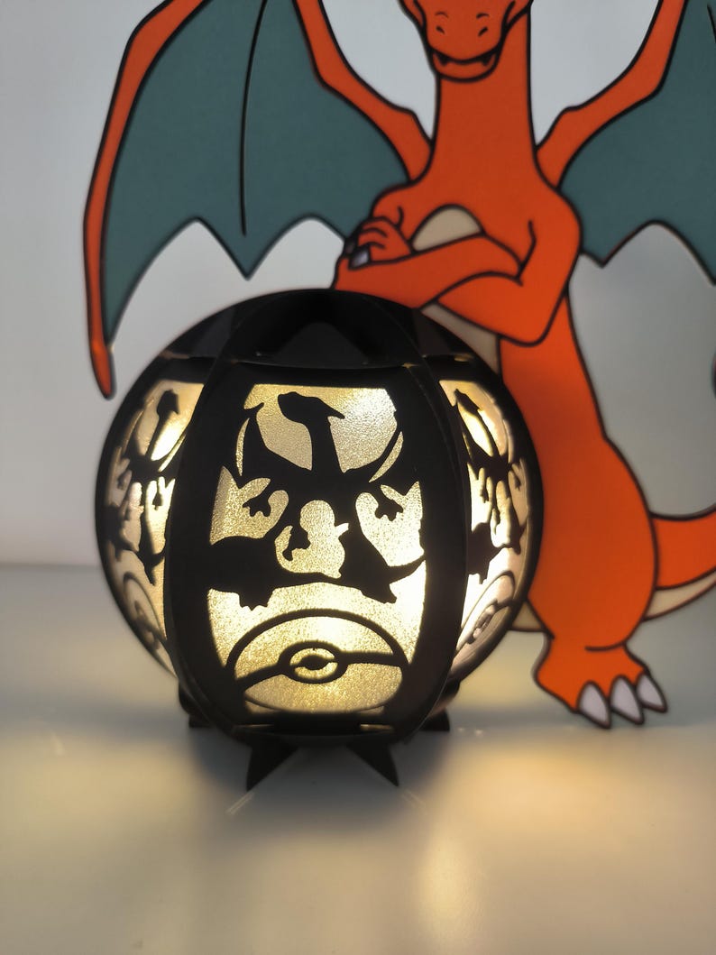 May include: A black light-up lamp shaped like a sphere with a silhouette of a dragon on the front. The lamp is lit and glowing. The lamp is next to a cartoon image of a red dragon.