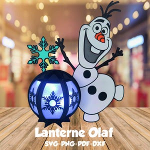 Puede incluir: Una linterna azul y blanca con un diseño de copo de nieve y un recorte de Olaf blanco. La linterna está iluminada con una luz azul. El texto "Lanterne Olaf SVG-PNG-PDF-DXF" está debajo de la linterna.