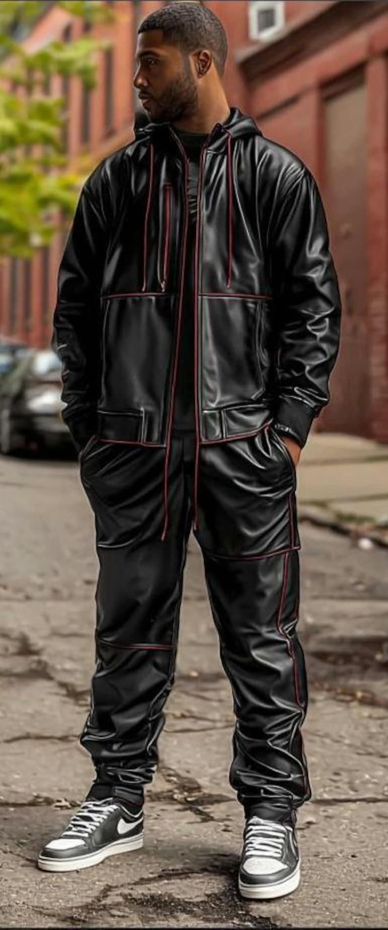 May include: Black leather-look tracksuit with red trim. The jacket has a hood and the pants have pockets. The outfit is paired with black and white sneakers. The person is standing on a city street.