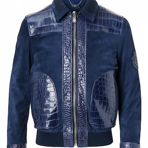 May include: A navy blue suede bomber jacket with crocodile-effect leather detailing. The jacket has a zip-up front, a collar, and a ribbed hem and cuffs. The crocodile leather is used on the shoulders, front panels, and cuffs.
