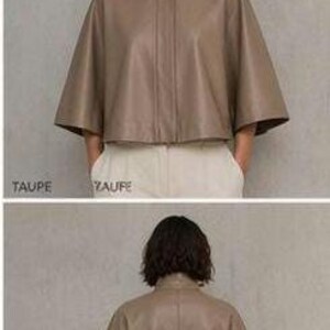May include: A taupe-colored leather cape jacket with a high collar and button closure. The jacket has wide, elbow-length sleeves and a cropped length. The model is wearing the jacket with white pants. The word "TAUPE" is printed at the bottom of the image.