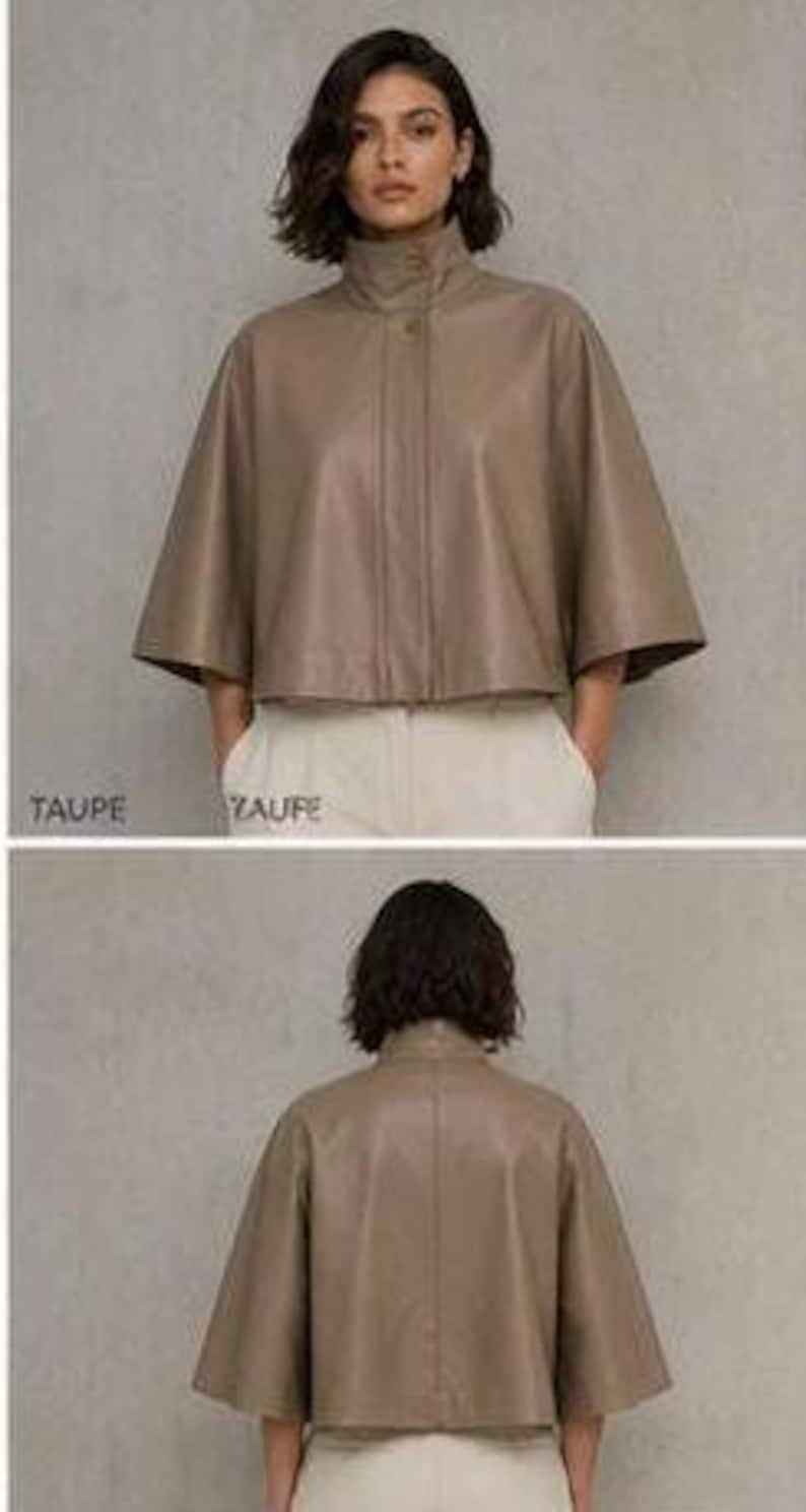 May include: A taupe-colored leather cape jacket with a high collar and button closure. The jacket has wide, elbow-length sleeves and a cropped length. The model is wearing the jacket with white pants. The word "TAUPE" is printed at the bottom of the image.