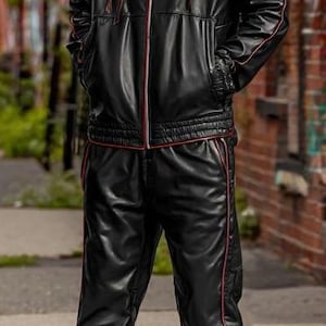 May include: Black leather tracksuit with red trim, featuring a hooded jacket and matching pants. The jacket has a zip closure and pockets. The outfit is worn with black and white high-top sneakers.