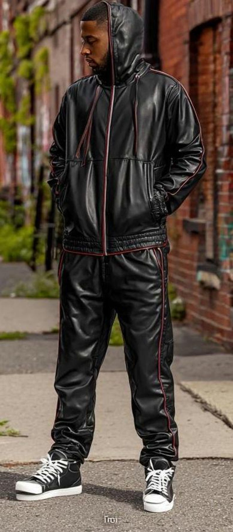May include: Black leather tracksuit with red trim, featuring a hooded jacket and matching pants. The jacket has a zip closure and pockets. The outfit is worn with black and white high-top sneakers.