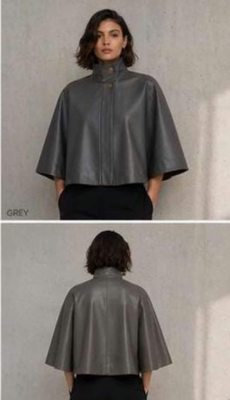 May include: A grey leather cape with a high collar and button closure. The cape has a wide, flowing silhouette and short sleeves. The word "GREY" is printed in the lower left corner of the image.