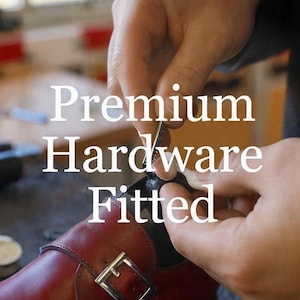 Może przedstawiać: Ciemnoczerwony sk&oacute;rzany but z paskiem z metalową srebrną klamrą. Tekst "Premium Hardware Fitted" jest nałożony w kolorze białym. But jest w trakcie obr&oacute;bki, wyraźnie widać cholewkę ze sk&oacute;ry oraz szczeg&oacute;ł metalowej klamry.
