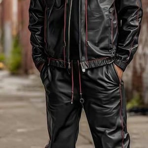May include: Black hooded jacket and matching pants with red trim. The outfit is made of a shiny material. The person is wearing white sneakers with black laces and a red sole.