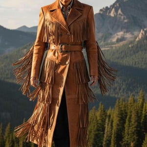 May include: A tan suede long coat featuring multiple tiers of long fringe on the chest, sleeves, and skirt. The coat has a double-breasted button closure, a matching belt with a metal buckle, and a wide collar. A tan cowboy hat is worn above.