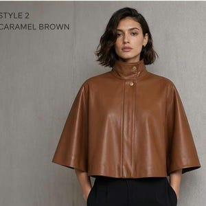May include: A caramel brown leather cape with a high collar and gold-colored buttons. The cape has a cropped length and a relaxed fit. The text "STYLE 2 CARAMEL BROWN" is visible in the upper left corner.