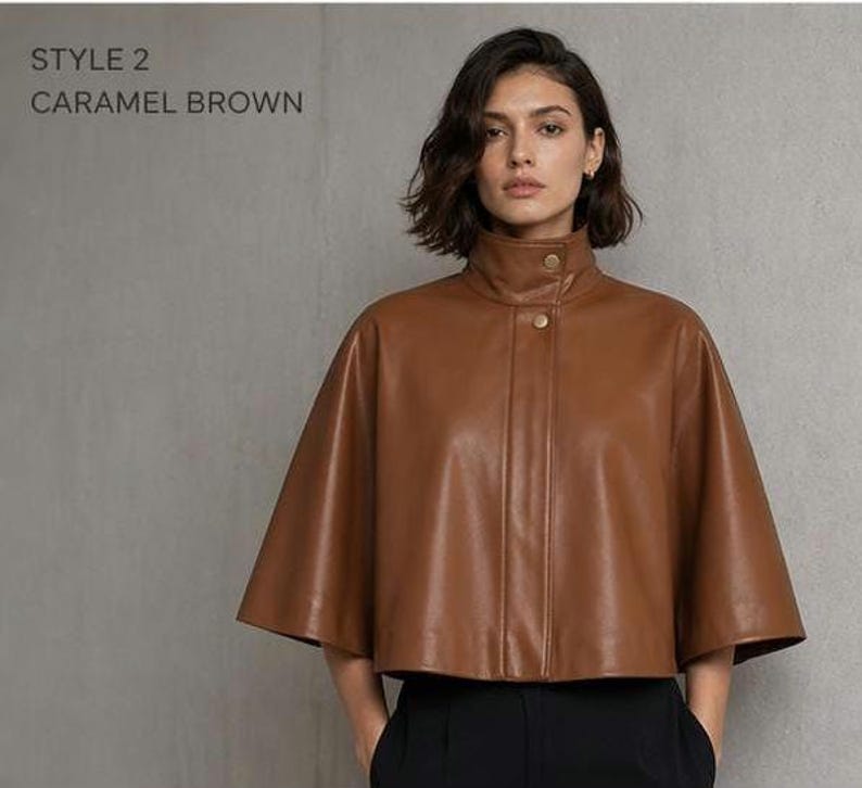 May include: A caramel brown leather cape with a high collar and gold-colored buttons. The cape has a cropped length and a relaxed fit. The text "STYLE 2 CARAMEL BROWN" is visible in the upper left corner.