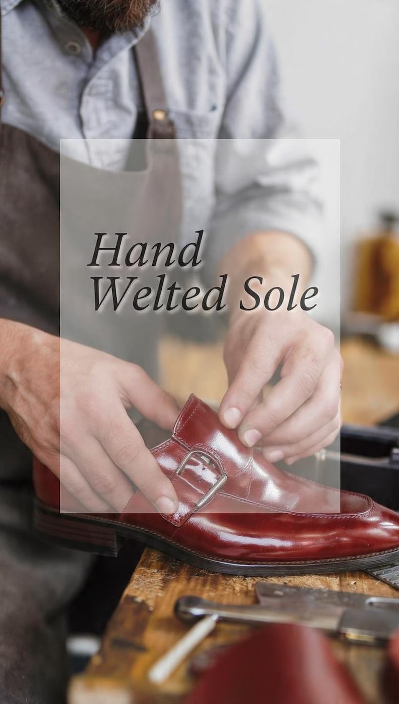 Może przedstawiać: Polerowany bordowy sk&oacute;rzany but z klamrą, srebrną metalową sprzączką i widoczną szytą podeszwą. Tekst "Hand Welted Sole" jest nałożony na obraz wyraźną, ciemną czcionką szeryfową na jasnym tle.