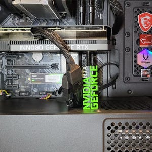 Peut inclure: Vue rapprochée de l'intérieur d'un boîtier d'ordinateur, montrant une carte mère noire avec une carte graphique NVIDIA GeForce RTX verte installée. Le boîtier est noir et argent et possède un panneau latéral transparent.
