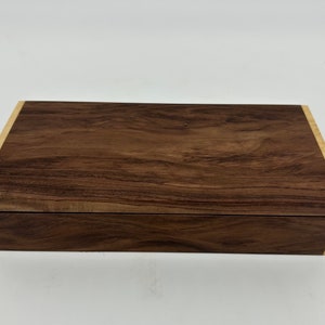 May include: A rectangular wooden box with a dark brown walnut finish and a light wood trim. The box has a hinged lid and is closed.