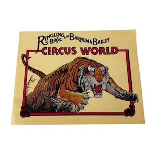 Peut inclure: Une affiche vintage de Ringling Bros. et Barnum & Bailey Circus World. L'affiche présente un tigre rugissant avec des rayures orange et noires, sur un fond crème. Le texte "Ringling Bros. and Barnum & Bailey Circus World" est affiché en rouge et noir.
