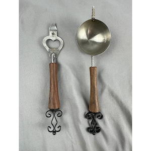 Könnte beinhalten: Zwei Vintage-Küchenutensilien: ein Flaschenöffner und eine Schöpfkelle. Der Flaschenöffner hat eine herzförmige Öffnung und einen Holzgriff. Die Schöpfkelle hat eine runde Metallschüssel und einen Holzgriff. Beide Werkzeuge haben dekorative schwarze Metallakzente.