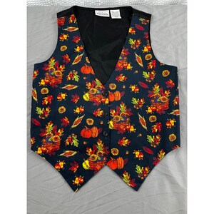 May include: A black vest with a colorful autumn-themed pattern. The design includes pumpkins, sunflowers, and fall leaves in shades of orange, yellow, and red. The vest has a black back and a button-up front.