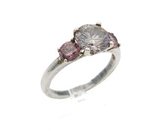 May include: A silver-toned ring featuring a large, clear, round-cut center stone flanked by two smaller, round-cut pink stones. The stones are held in place by metal prongs on a smooth, polished silver-toned band that tapers toward the setting.