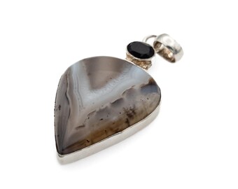 May include: A teardrop-shaped pendant featuring a polished grey and white banded agate stone set in a silver-toned metal frame. A small, oval-cut black gemstone is mounted above the main stone, connected to a silver-toned metal bail for hanging.