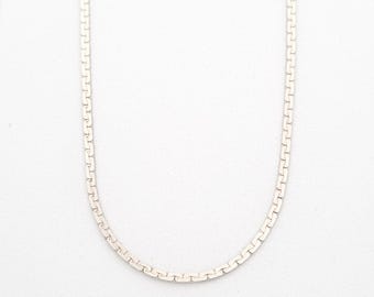 May include: A silver-colored necklace with a flat, rectangular link design. The chain is displayed against a white background, showcasing its simple yet elegant style. The necklace is a delicate piece of jewelry.