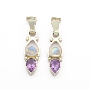May include: A pair of silver earrings featuring a teardrop-shaped purple amethyst stone at the bottom and a round, iridescent moonstone above. The earrings have a unique, elongated design with a post-back closure.