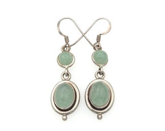 May include: A pair of dangle earrings featuring two light green oval-shaped stones set in silver metal. Each earring has a smaller round stone at the top and a larger oval stone at the bottom, connected by silver links with a hook-style closure.