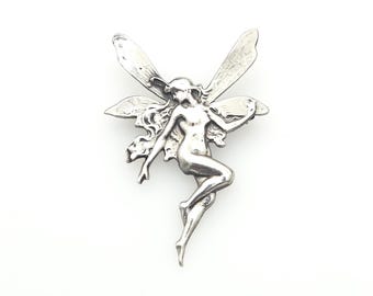 May include: A silver-toned metal brooch shaped like a winged figure with long flowing hair. The figure is depicted in a dynamic, mid-air pose with arms extended and legs bent, featuring detailed wings that span horizontally behind the torso.