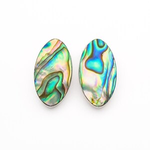 Peut inclure: Deux boucles d'oreilles ovales avec des coquillages d'ormeau irisés sertis dans du métal argenté. Les coquillages présentent un mélange de teintes vertes, bleues et jaunes. Les boucles d'oreilles sont présentées sur fond blanc.