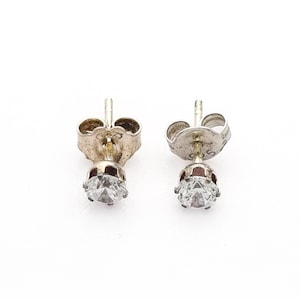 May include: A pair of silver stud earrings featuring a clear, round gemstone. The earrings have a post and butterfly clasp. The gemstones are set in a four-prong setting. The earrings are shown against a white backdrop.