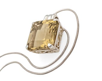 May include: A square-cut, translucent yellow gemstone pendant set in a silver-toned metal frame with intricate scrollwork detailing on the sides. The pendant hangs from a thin, flexible silver-toned snake chain necklace against a plain background.