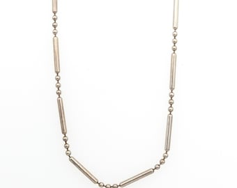 May include: A silver-toned metal chain necklace featuring a repeating pattern of small spherical beads interspersed with elongated cylindrical bar links. The design consists of alternating sections of round ball chain segments and smooth metal tubes.