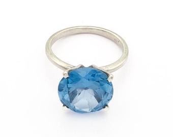 May include: A silver ring featuring a large, round, light blue gemstone. The gemstone is faceted, catching the light and creating a sparkling effect. The ring band is a simple, polished silver.