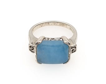 May include: A silver ring featuring a rectangular, smooth, light blue stone set in a metal frame. The band displays intricate cut-out detailing on the sides and is stamped with 925 on the interior, indicating sterling silver composition.