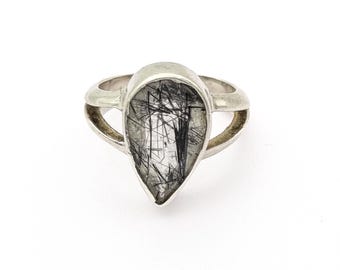 May include: A silver ring featuring a teardrop-shaped stone with black inclusions. The ring has a split band design, with the stone set in a bezel setting. The stone's pattern resembles a network of black lines.