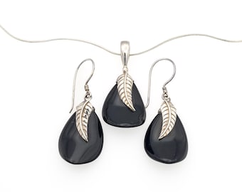 May include: A jewelry set consisting of a pendant on a thin silver chain and two matching drop earrings. Each piece features a smooth, black, teardrop-shaped stone accented with a silver leaf-shaped bail that sits atop the upper curve of the stone.