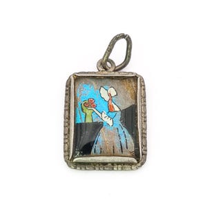 Peut inclure: Pendentif en argent vintage avec un cadre rectangulaire. Le pendentif présente une peinture miniature d'une figure en robe bleue tenant des fleurs. La peinture a un fond bleu et est encadrée par une bordure argentée décorative.