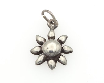 May include: A silver-toned metal charm shaped like a sun with a smooth, rounded center and eight radiating petals. The charm features a small, open circular jump ring at the top for attachment, showcasing a polished finish with subtle dark oxidation.