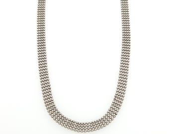 May include: A silver-toned necklace featuring a multi-strand chain design composed of numerous small, uniform metallic spheres arranged in a dense, grid-like pattern that creates a textured, flexible band with a consistent width throughout.