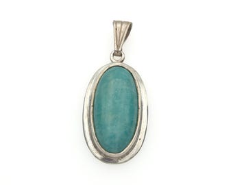 May include: An oval pendant featuring a smooth, teal-colored stone set within a polished silver-toned metal frame. The pendant includes a vertical, ribbed metal bail at the top, designed for attachment to a chain or cord for wear as a necklace.