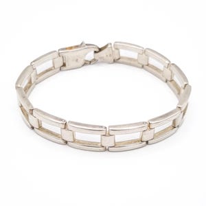 May include: A silver-colored bracelet with a rectangular link design. The bracelet has a clasp closure. The links are approximately 0.75 inches long and 0.25 inches wide. The bracelet is on a white background.