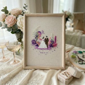 May include: A framed embroidered artwork featuring a couple in wedding attire, surrounded by purple and pink floral accents. The artwork includes the date "2026.01.07" and is set against a neutral linen background, framed in light wood.