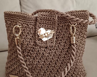 May include: A brown crocheted tote bag with a gold heart-shaped clasp and rope handles.