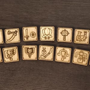 Puede incluir: Un conjunto de 14 fichas de madera con varios símbolos y diseños, incluyendo espadas, escudos y otras armas. Las fichas son todas del mismo tamaño y forma, y están dispuestas en una cuadrícula.