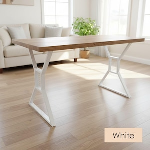 Op de afbeelding: Een rechthoekige houten eettafel met een lichtbruin oppervlak. De tafel heeft witte metalen poten met een geometrisch ontwerp. Het woord "White" wordt weergegeven in een beige rechthoek onderaan de afbeelding. De tafel staat in een goed verlichte kamer.